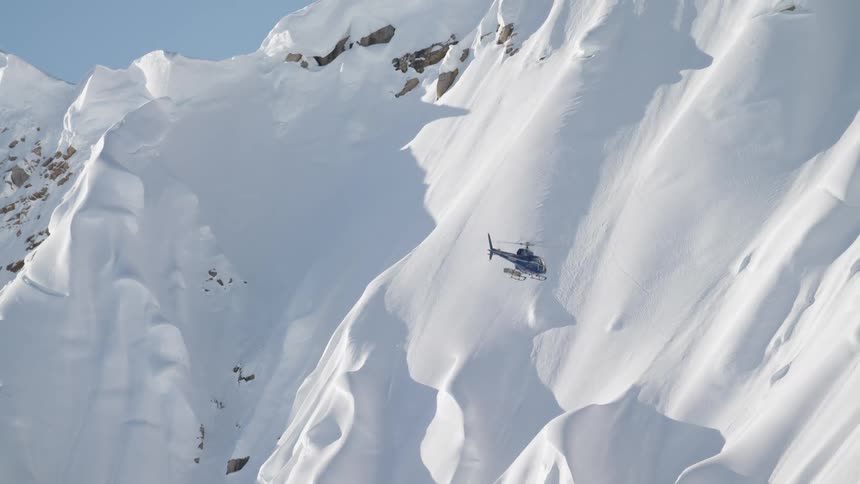 A helicopter is flying by mountains covered in snow