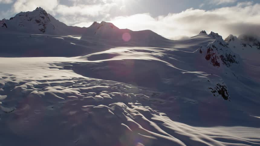 The sun shines and glares over a rocky snow covered ridge