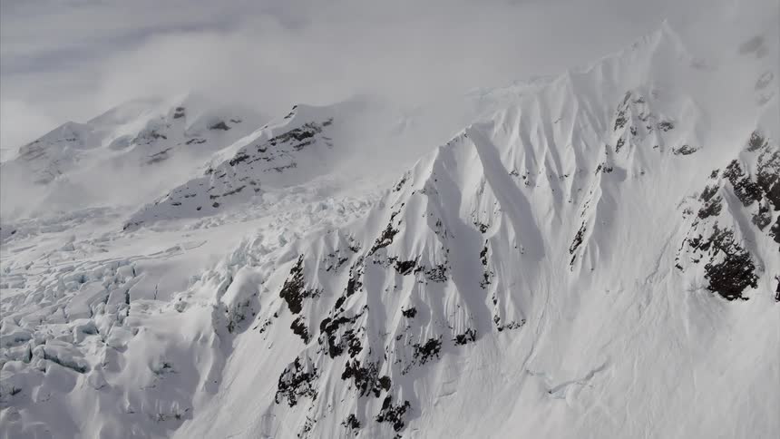 Clouds hang over and cover the snow covered mountain ridge and slope