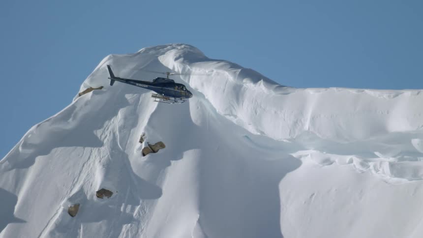 A helicopter hovers near a snow covered mountain peak