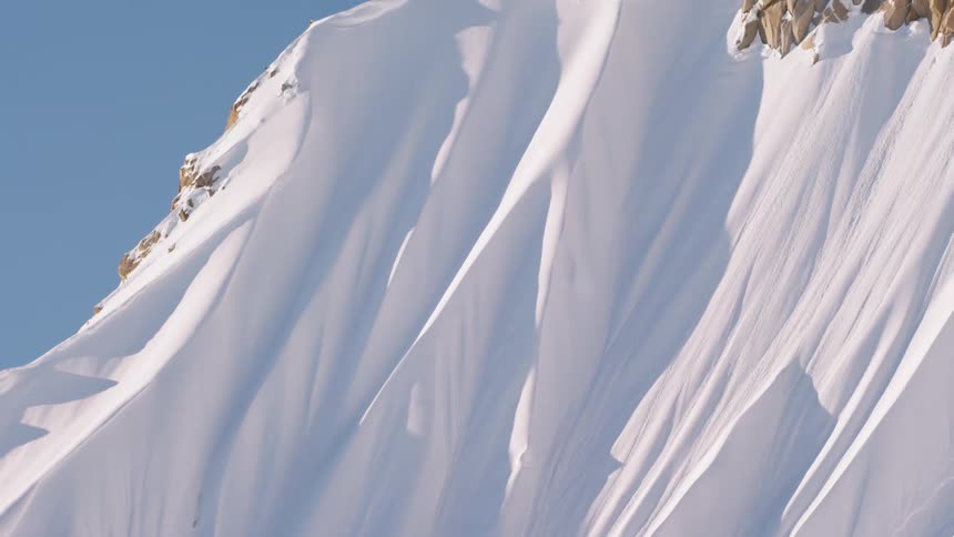 Snow drifts drape the slope of a large mountain