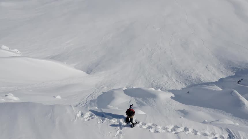 Snowboarder stands on ridge overlooking tall downhill slope