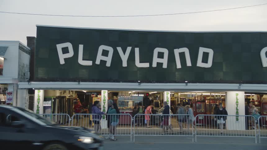 People milling about the front of an arcade separated from the road by metal barricades