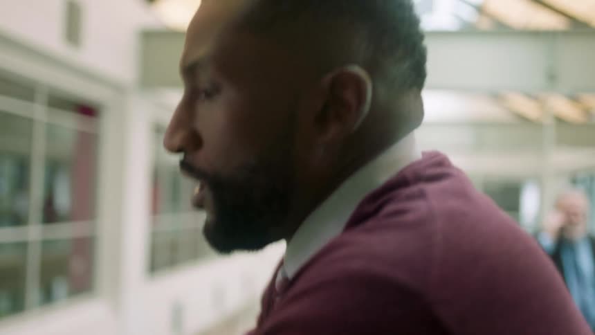 A black man strolls through an office building while talking on a smartphone