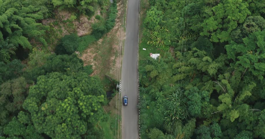 Blue car driving down left side of rural road through forest
