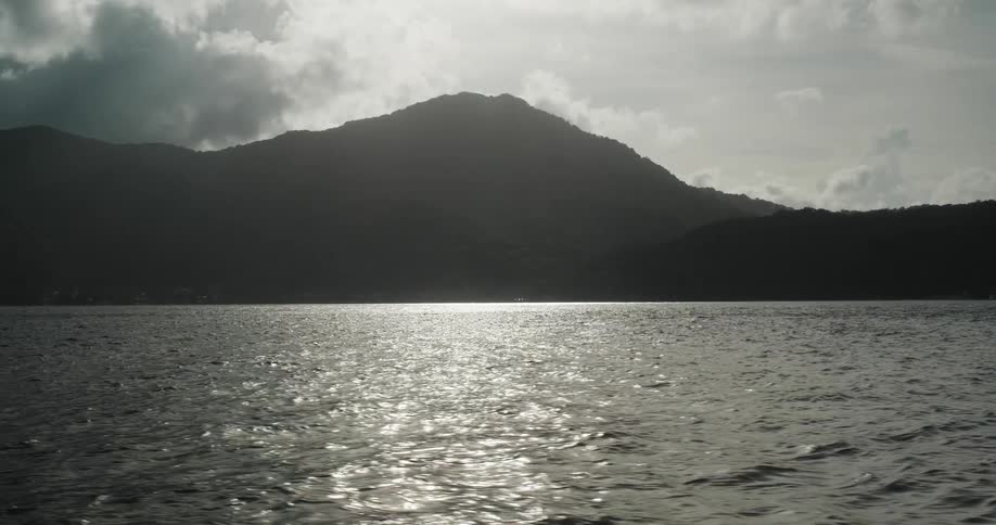 Sunlight peaks from behind a mountain near the ocean