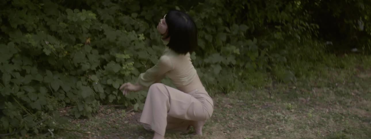 Woman wearing vintage clothes dances while kneeling on the floor outdoors