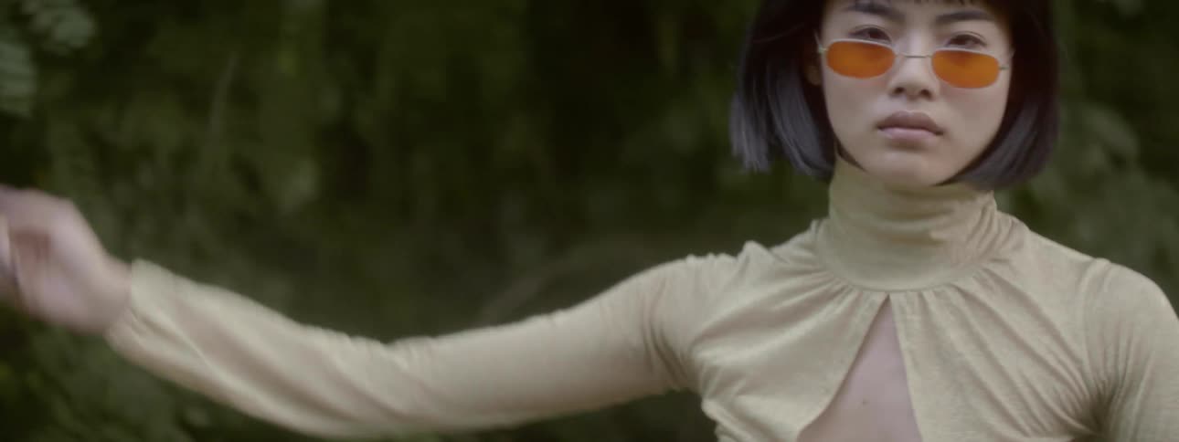 Young asian woman with serious expression spins and dances in front of woods