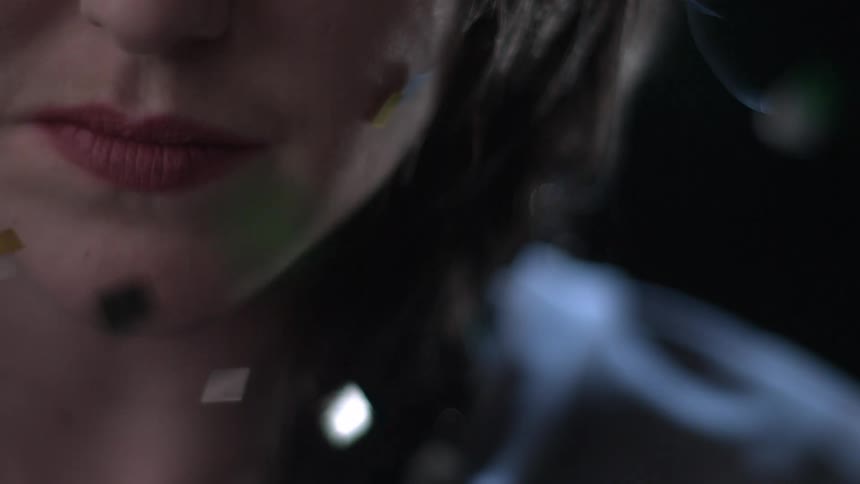 A white woman stands still as glitter floats in the sky around her face