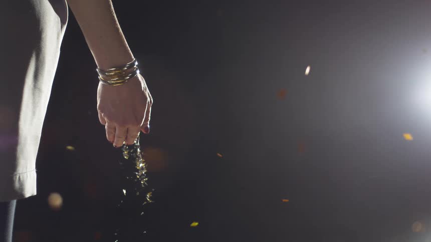 A white woman stands still while glittery objects spill out of her hand