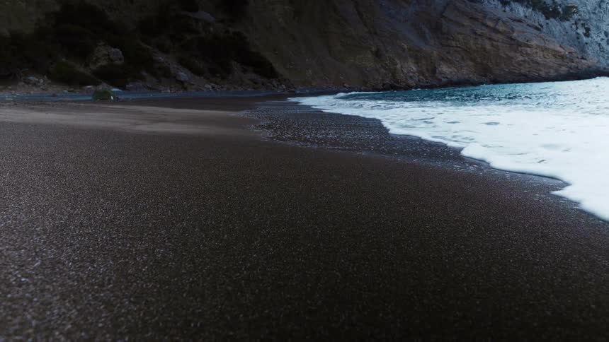 A sandy beach with waves with a cliff in the background
