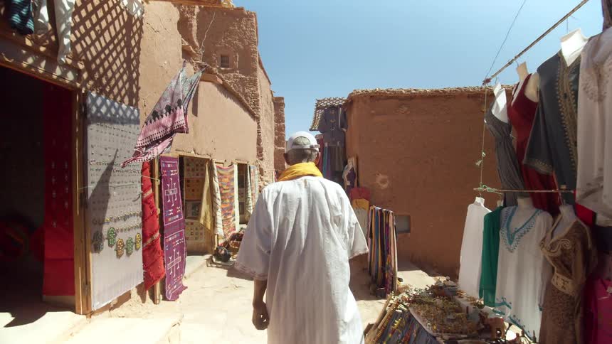 Man walks down narrow street bordered by shops displaying wares on outdoors