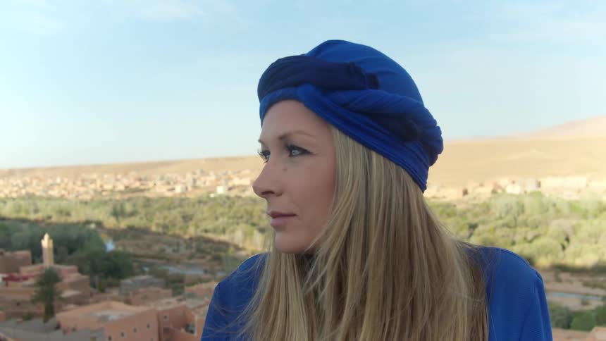 Woman in blue headscarf sits above village in desert