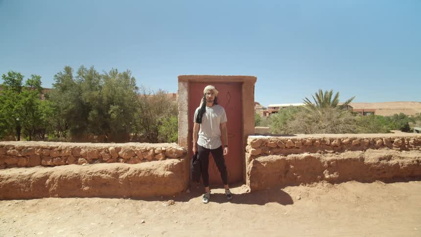 Man standing in front of door and ruins in desert gives thumbs up and smiles