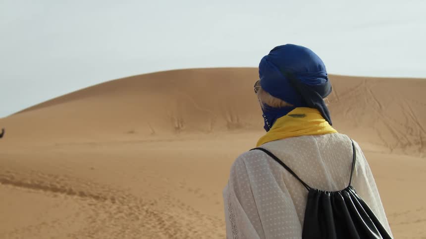 Woman with blue scarf covering head and face walking through vast desert