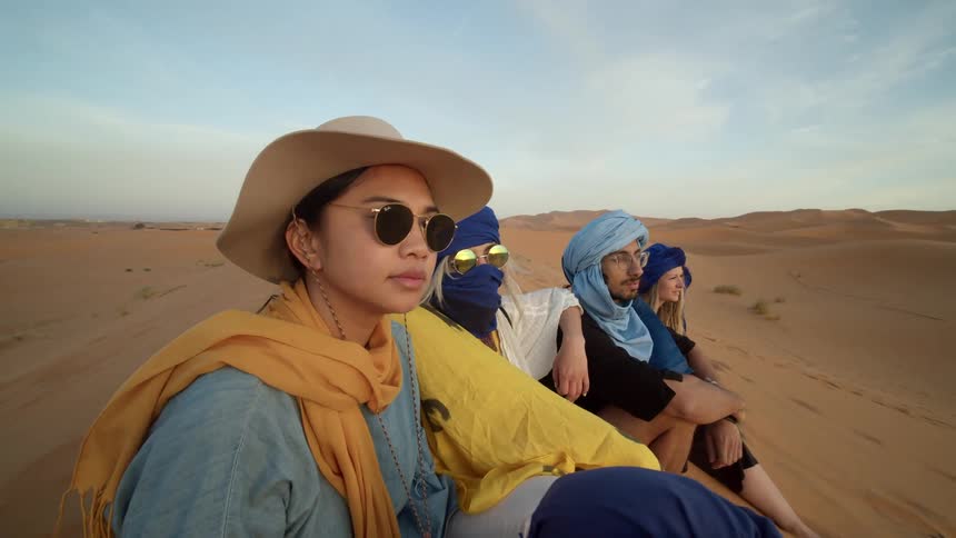 A group of people sit together on a sand dune in the desert