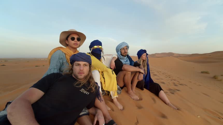 A small group of people sit on the dune in the desert