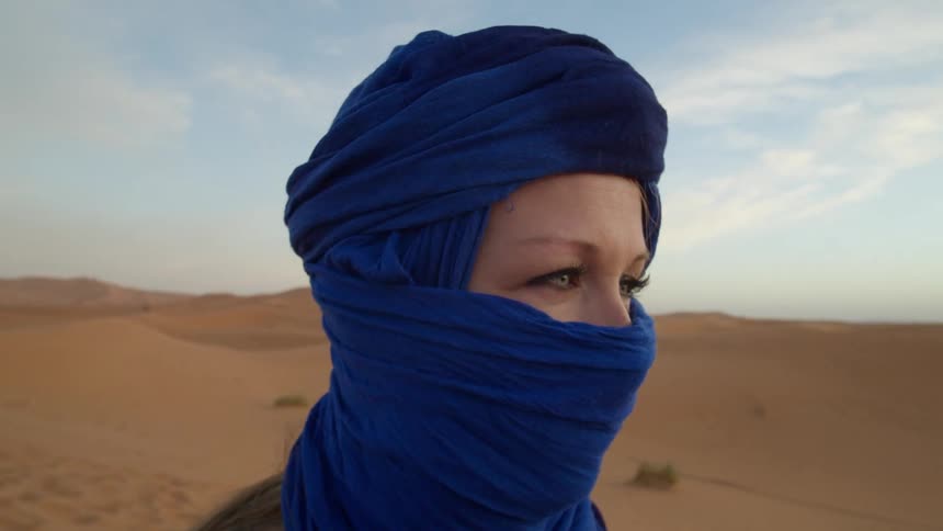 Woman wearing blue headscarf covering face stands in vast desert