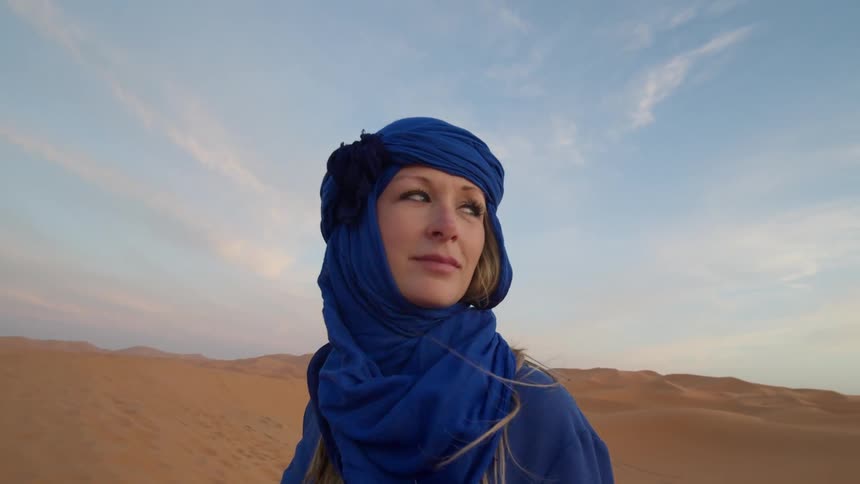 Blue eyed woman wearing a blue scarf looks around in the desert