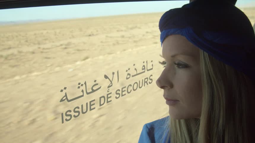 Woman looks out window of bus driving through desert