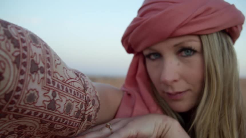 A woman wearing a scarf turban raises her arm as she poses in the desert