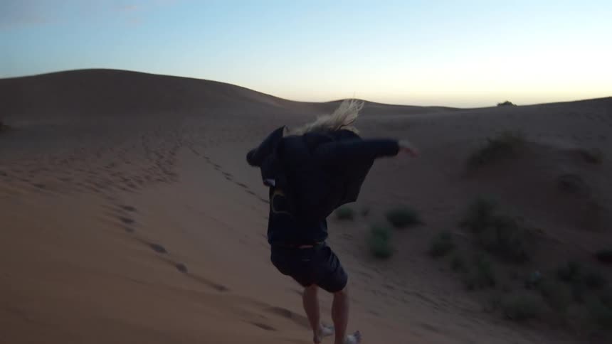 Young man jumping down from a sand dune on a desert at sunset