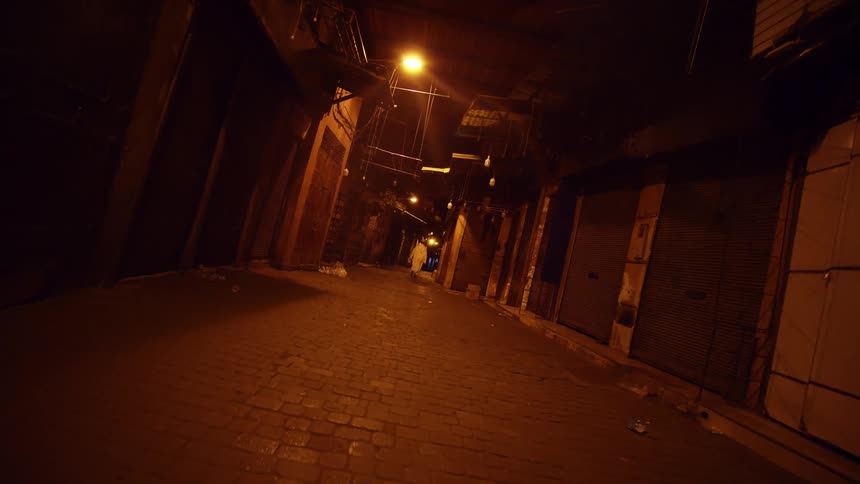 A person in a white robe walking through a dimly lit and raggedy alleyway at night