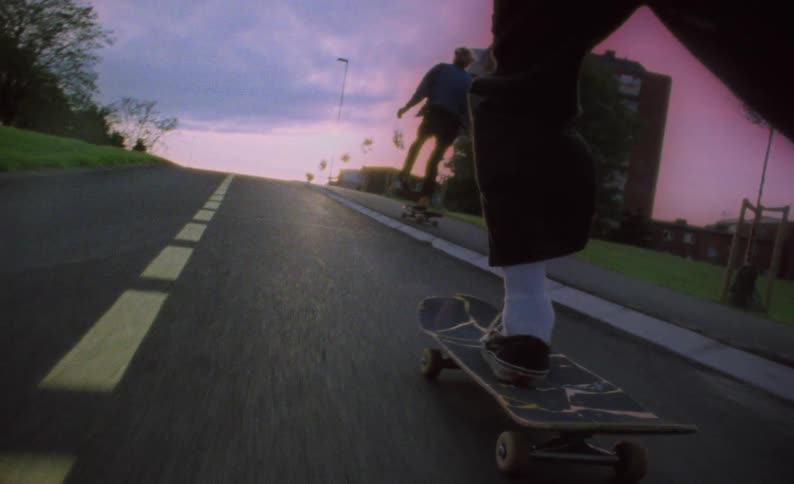 A boy pushes off the street as he rides his skateboard behind his friend at sunset