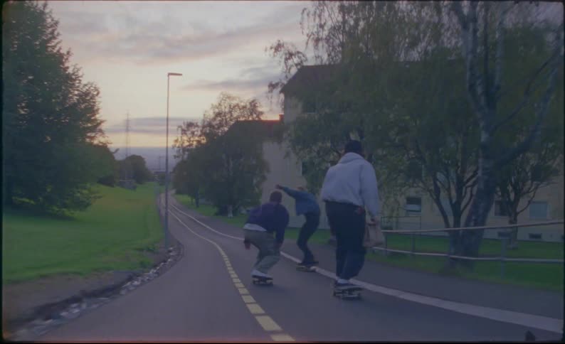 Three white teens race down a park path on skateboards