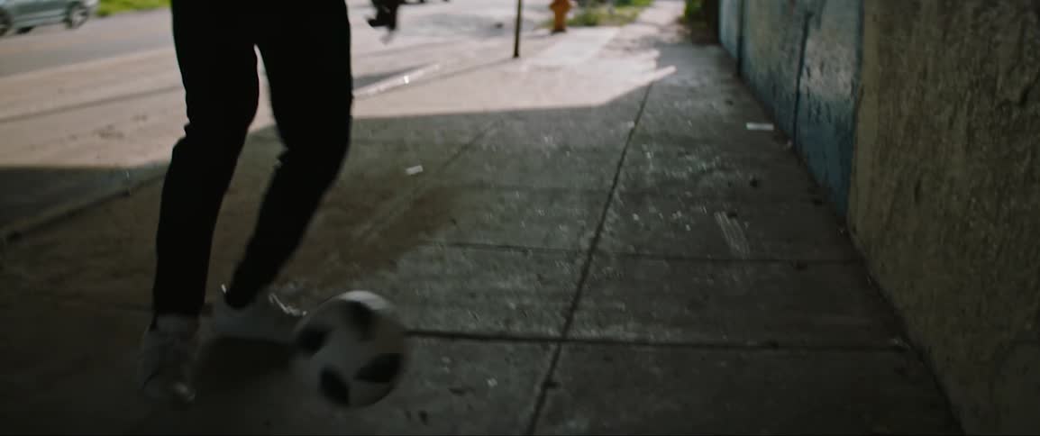 A man is kicking the soccer ball under the overpass