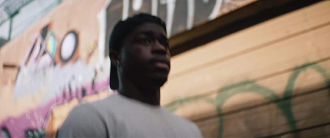 Young black man walks down graffiti covered street carrying jacket and reusable grocery bag
