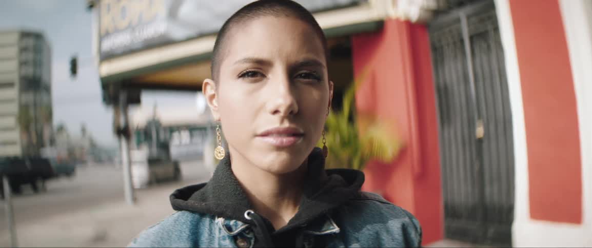 Woman with shaved hair stands on the street of a city