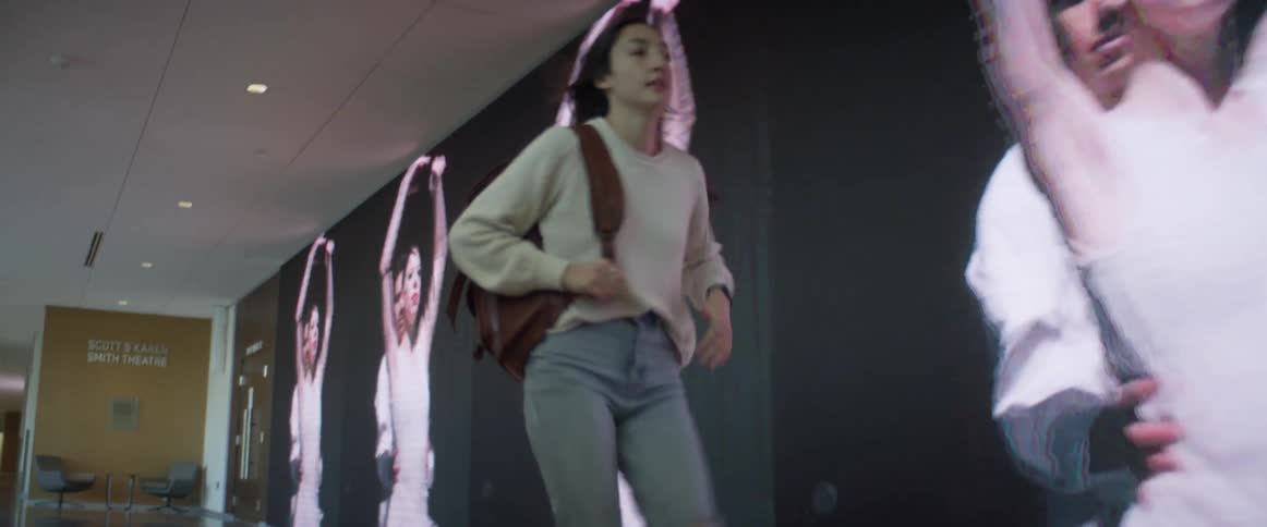A teenager runs down a hallway as she looks at her watch
