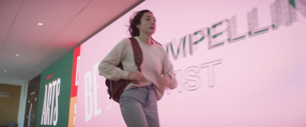A young woman runs through a mall with a backpack looking at her watch that shes running late
