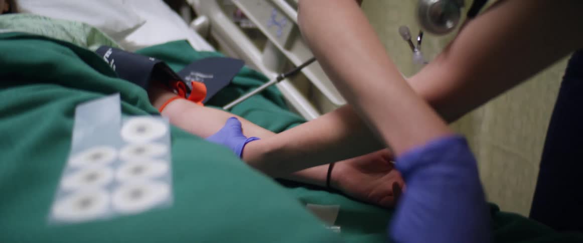 A nurse frantically tries to draw blood from a patient in a hospital bed