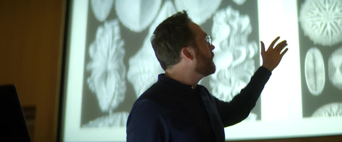 A man standing looking at a slide and talking