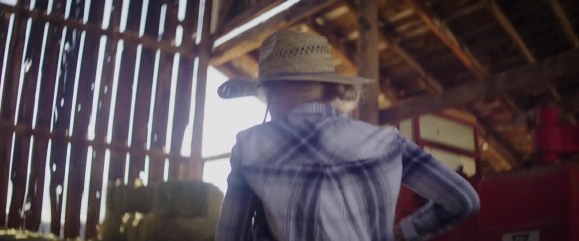 A female farmer lifts and moves hay bales inside a barn