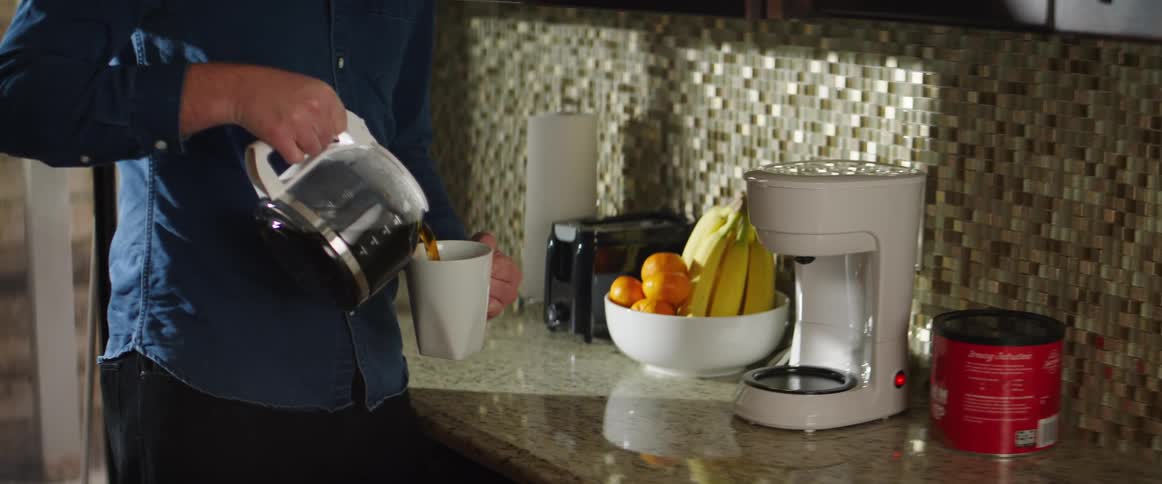 Man pours coffee from coffee maker into mug