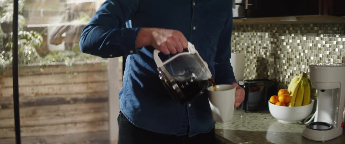 Man in kitchen pours coffee from coffee maker into mug