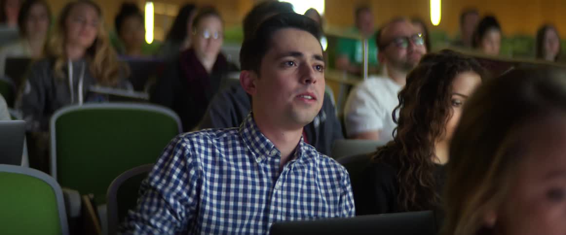 A male student works on his laptop in a lecture hall and then raises his hand