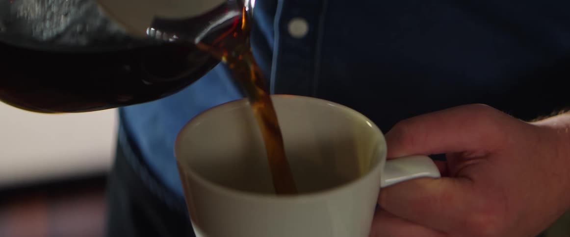 A white man pours coffee into a white mug