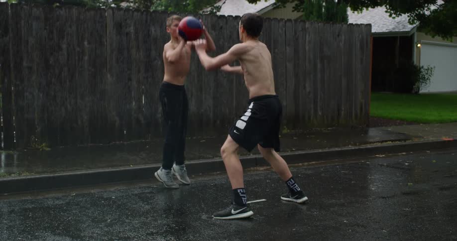 Friends play basketball in neighborhood streets while raining