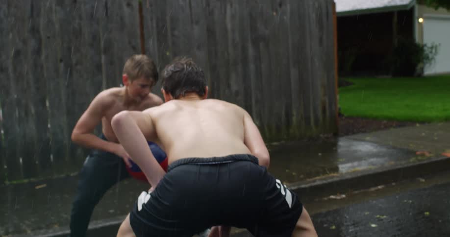 Boys playing pickup basketball game in the rain on neighborhood street