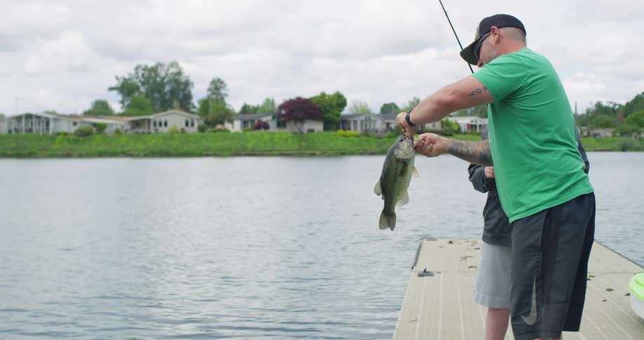 A man and a child go fishing off of a dock at a lake