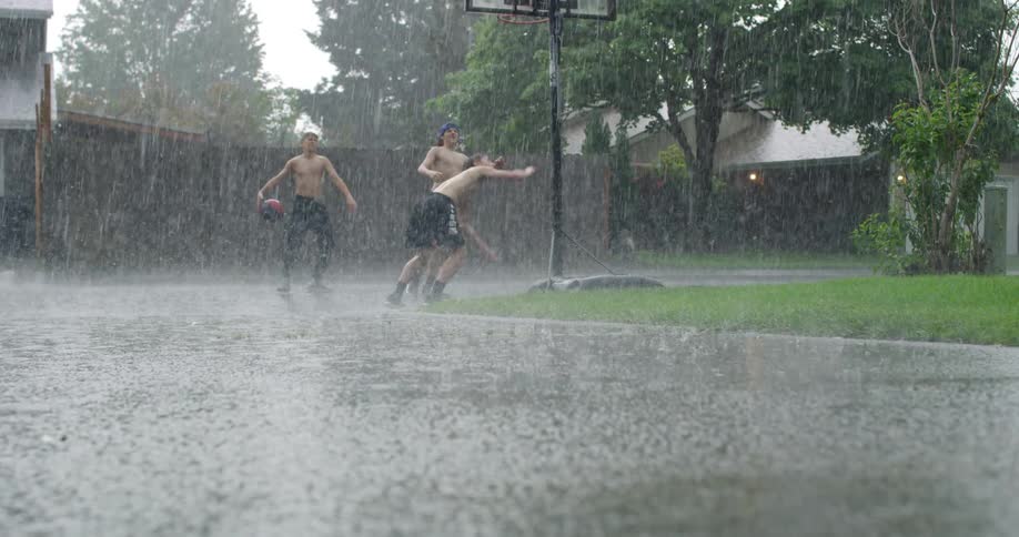 Three people are playing basketball in the rain