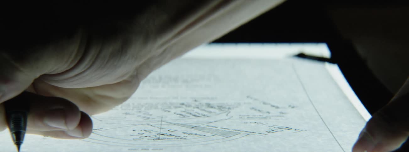 Person drawing schematics by hand with a pen on a backlight surface