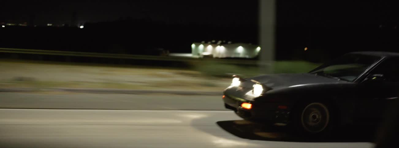 A black sports car speeds down a highway at night