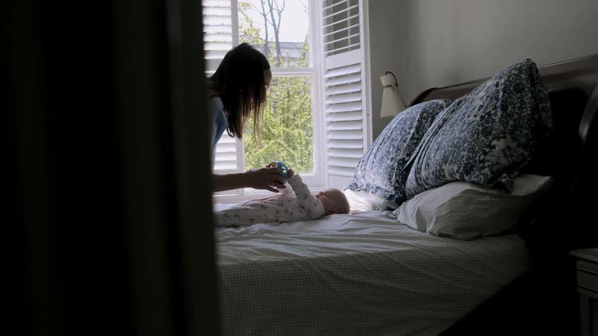 A mother plays with her infant in bed