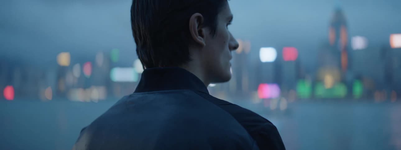 A man looks over the water towards the buildings at dusk