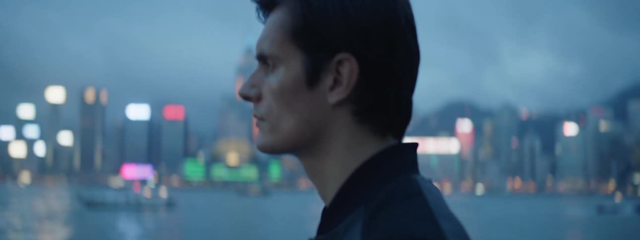 A man stands in front of the water with the city skyline in the distance